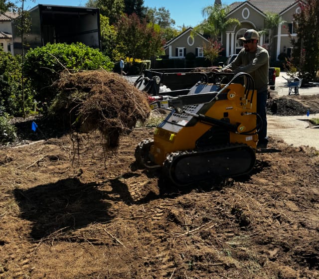 Skid loader removing dirt and roots from a yard